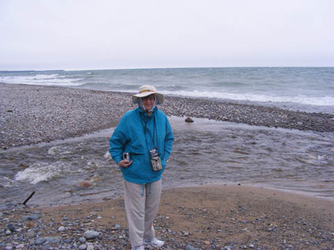 Gail standing in front of a small stream flowing into Lake Superior. She's bundled up against the cold wind.