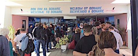 Backs of passengers passing under the Welcome to Bonaire sign