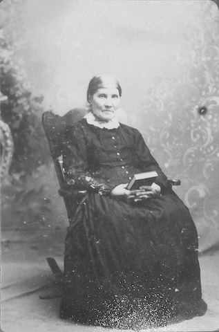 Eva Anderson is sitting in a rocking chair and holding a book in both hands