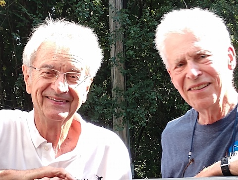 The white-haired men are in the sun and looking at the camera