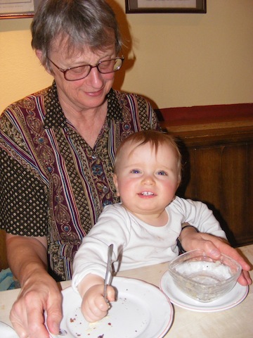 Gail is sitting at a restaurant table with a smiling               Felix in her lap. Felix is looing right at the camera.