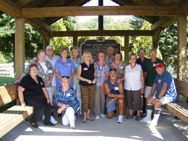 Fifteen members of the 8th grade class of 1960
               pose in the shelter dedicated to the First Swedish
               Settlers in Wisconsin. Our host Debbie Miller 
               is sitting on the left.