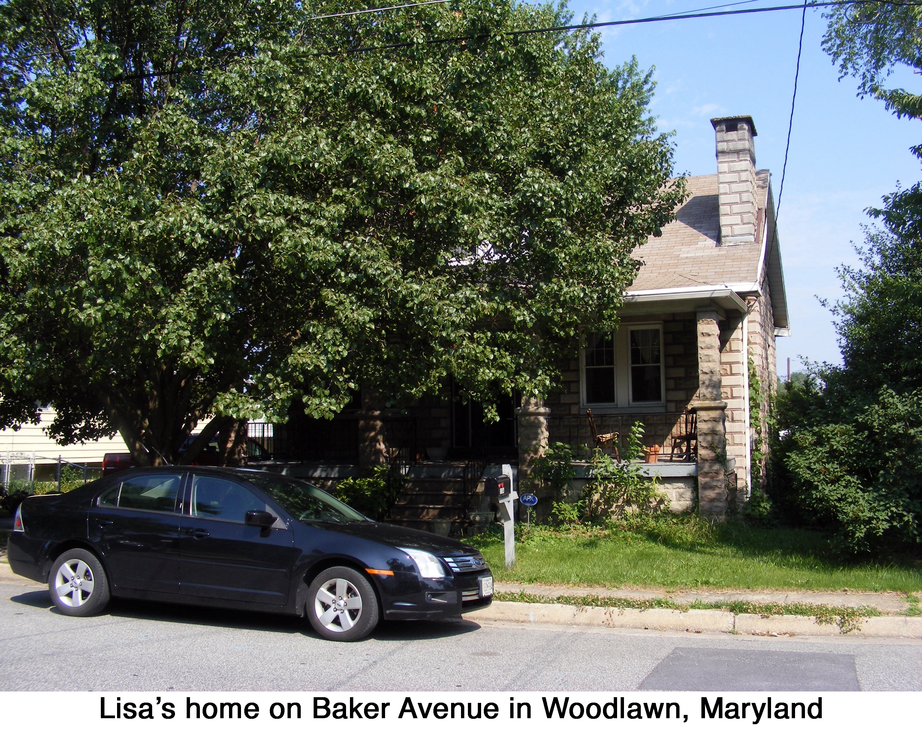 The stone-veneered house shaded by a tree and seen from across the street