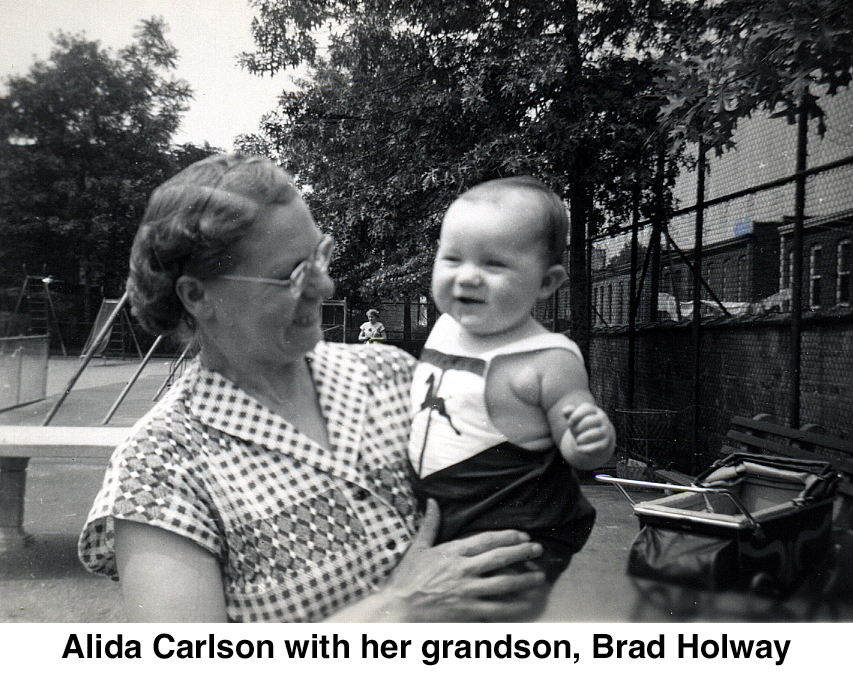 Alida is holding Bardley and smiling at him in an urban playground.
            He looks happy.
