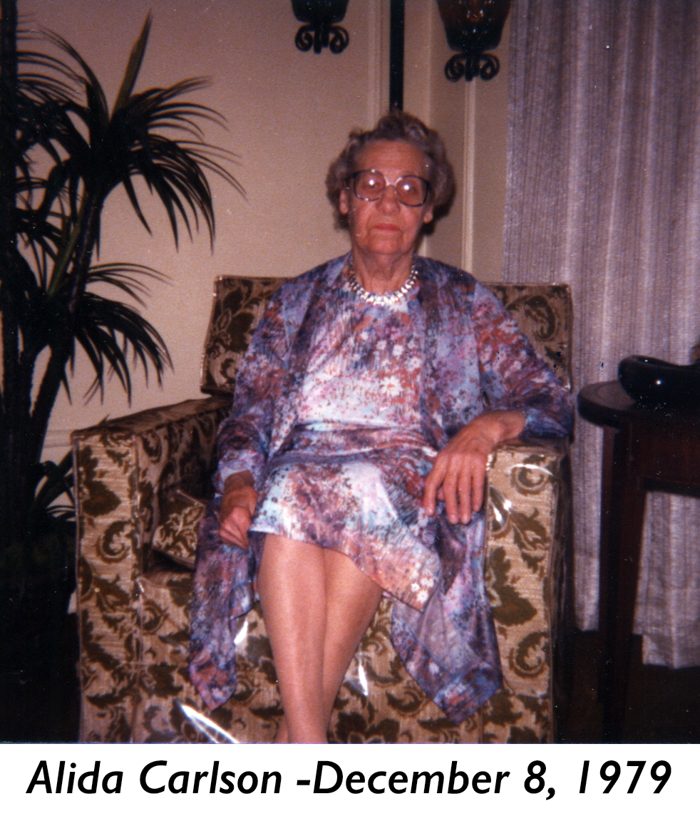 Alida is wearing a colorful dress and sitting in a upholstered chair