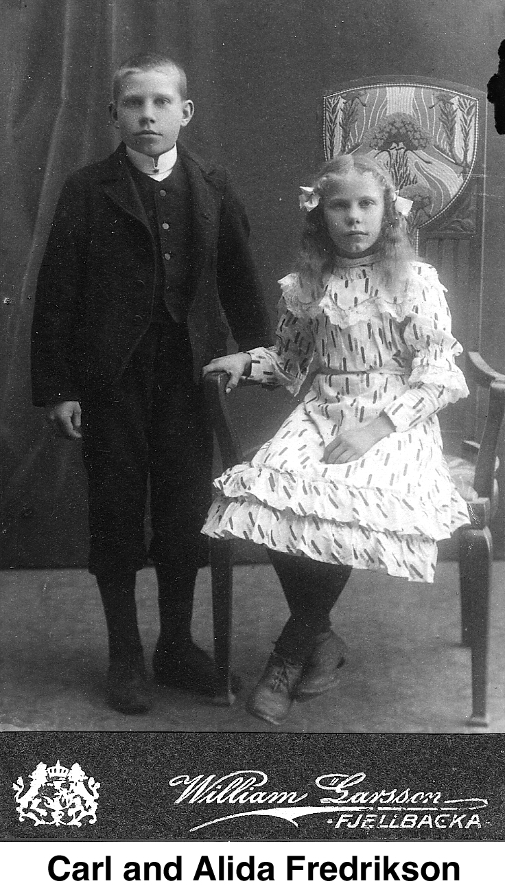 Carl is wearing a suit with a vest and standing beside the 
            chair in which his sister sits.