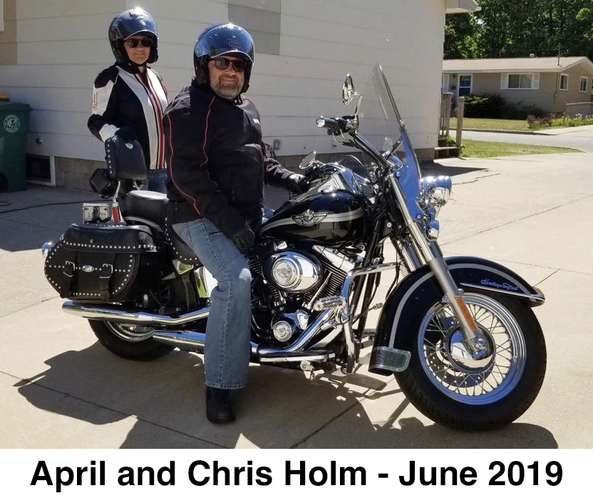 April and Chris are sitting on the motorcycle and are wearing full gear.