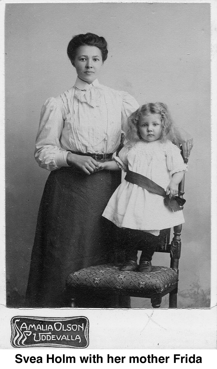 Svea has long, curly blond hair. She’s wearing a white 
       dress and standing on a chair. Frida is standing beside her.