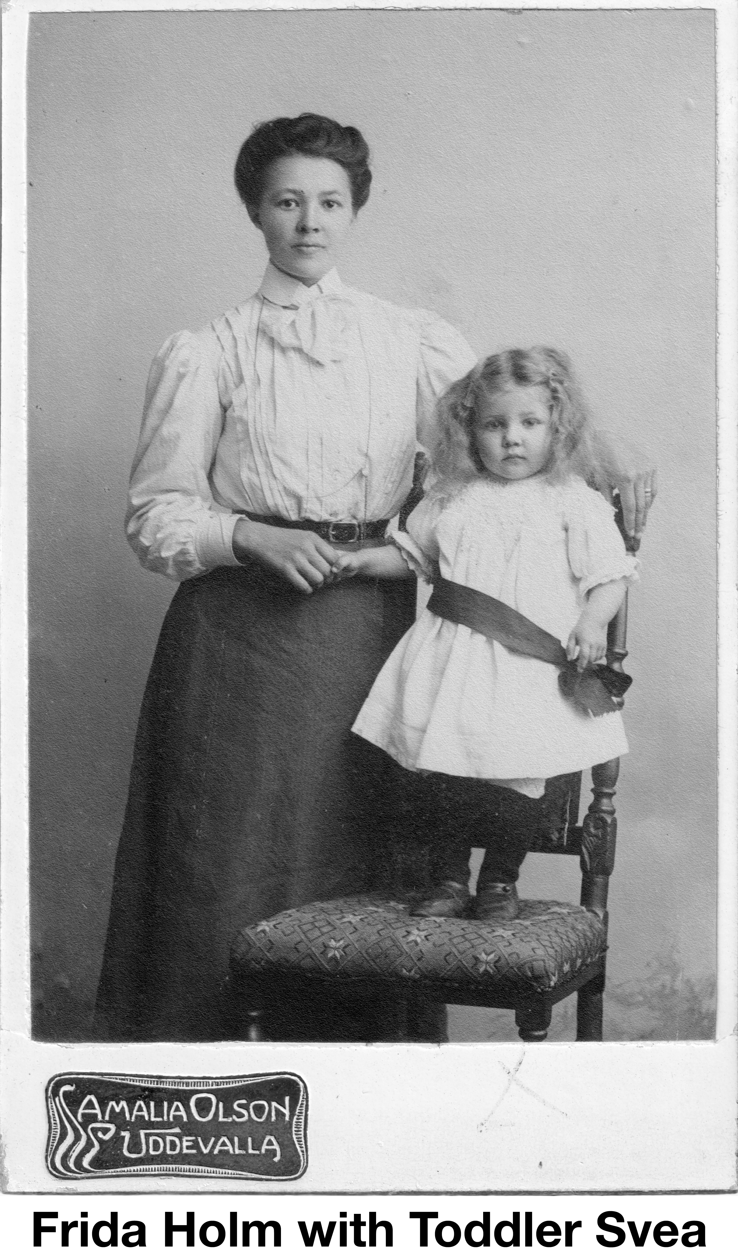 Frida is standing and holding Sveas hand. Svea is standing on a chair.