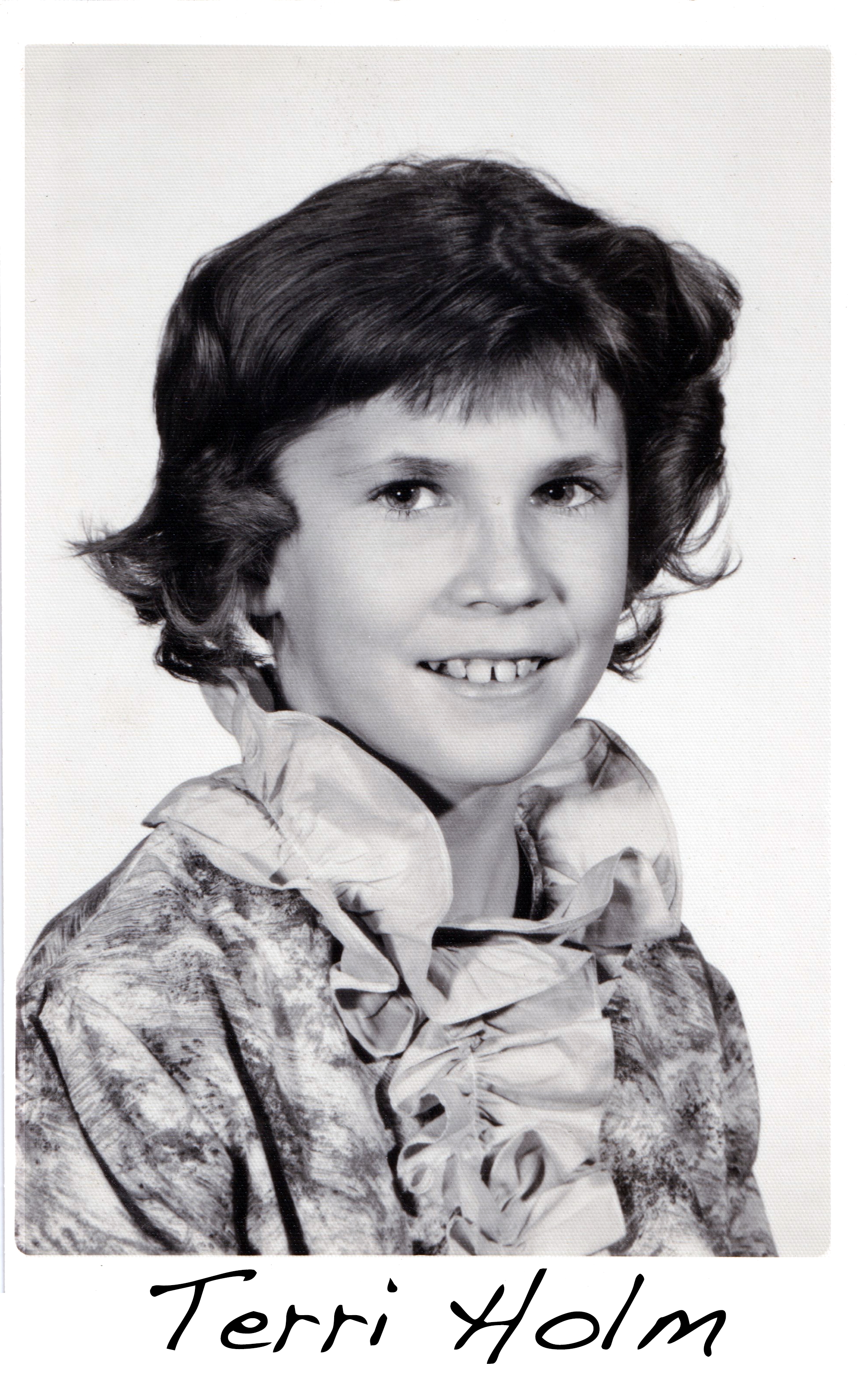 A black-and-white photo of Terri Holm wearing a frilly blouse and 
       with curls in her hair