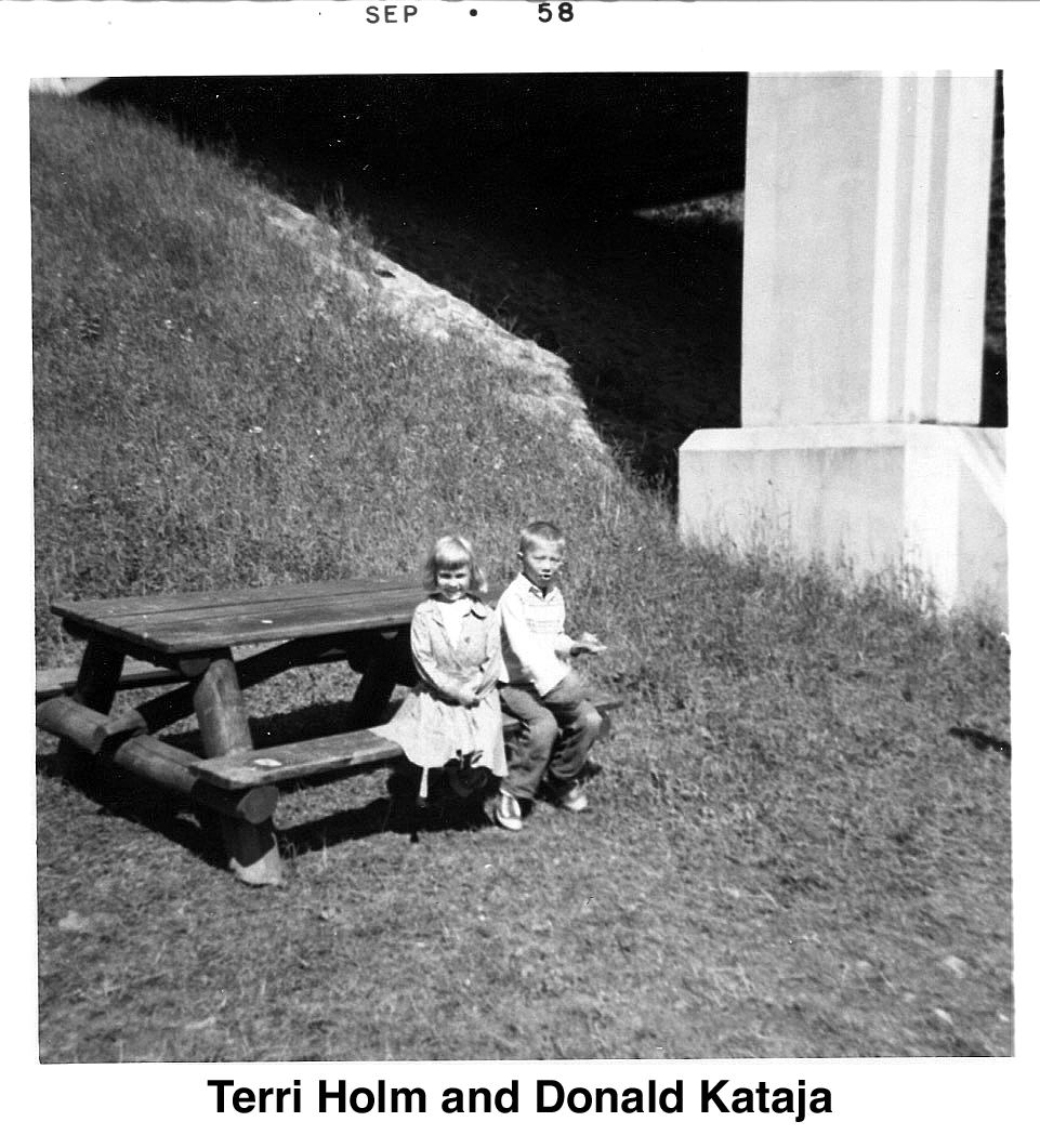 The two are sitting at a picnic table with the bridge supports in the background