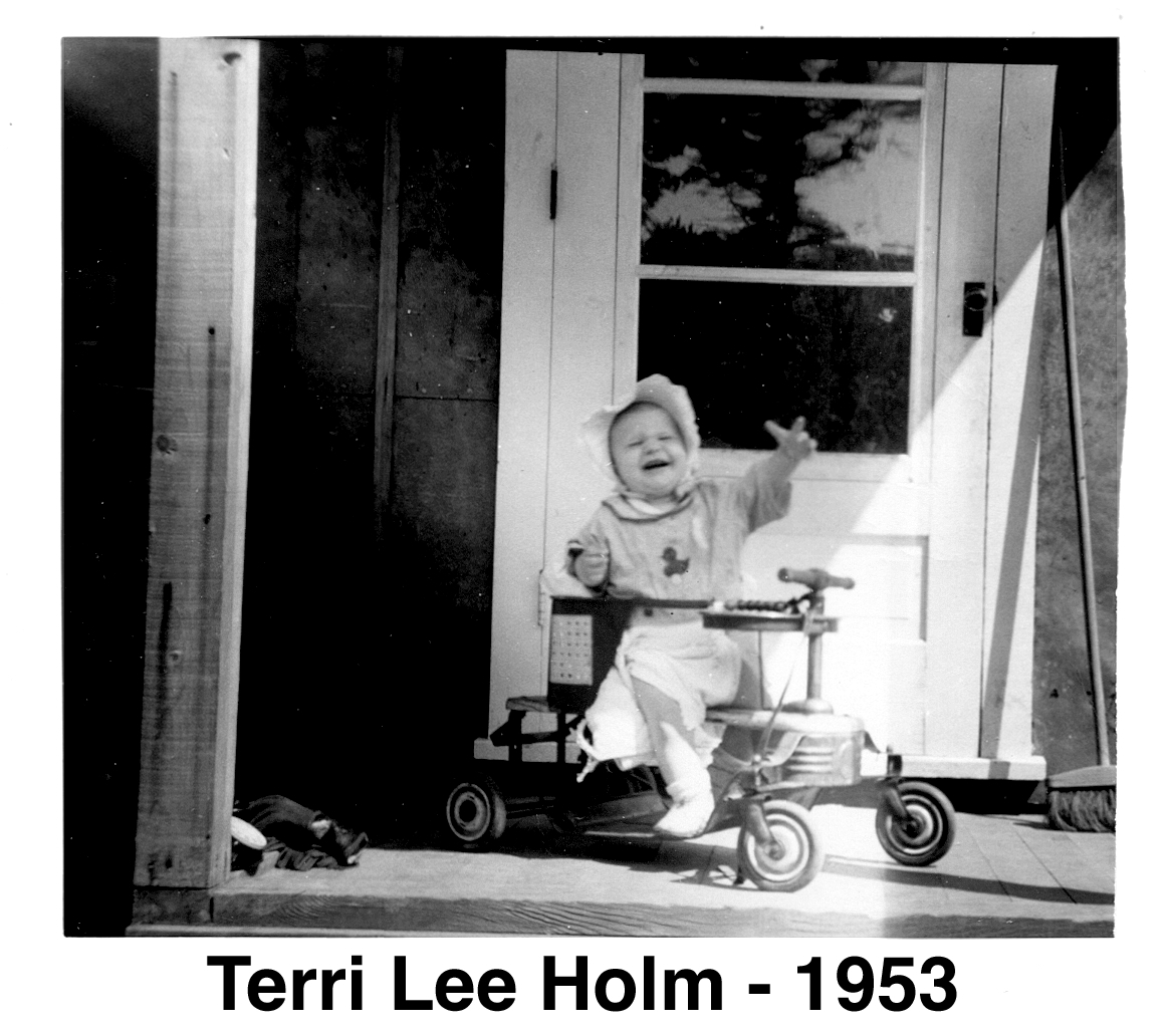 Terri sits in a walker with the door behind her. 
           She is reaching toward the photographer. 