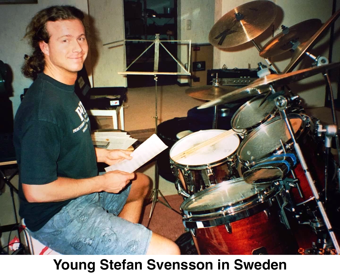 Stefan is sitting at a drum kit and smiling at the camera