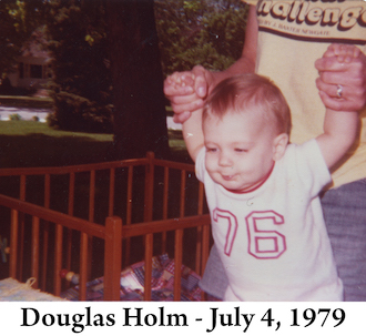 Gail is holding Doug’s hands in the yard of his Paton grandparents 