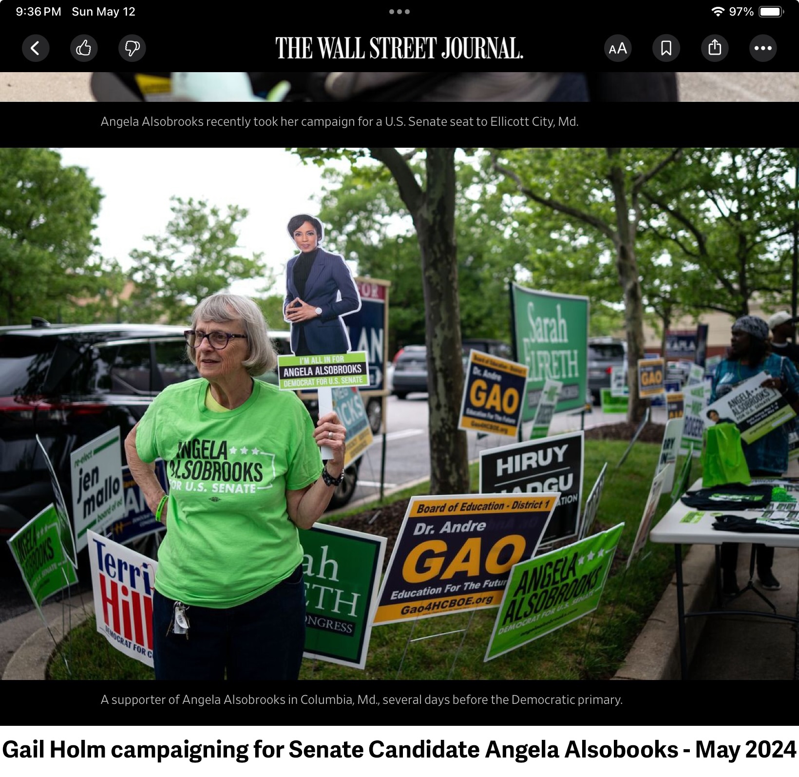 Gail is holding a cardboard image of the candidate, Angela Alsobrooks, and 
          standing in front of a lot of campaign signs