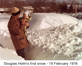 Warmly dressed Doug is held amidst the snow 