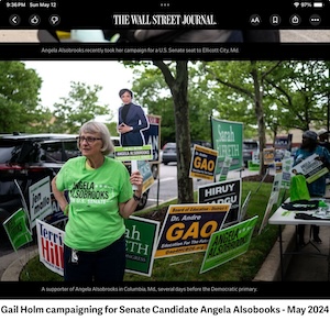 Gail is holding a cardboard image of the candidate, Angela Alsobrooks, and 
          standing in front of a lot of campaign signs.