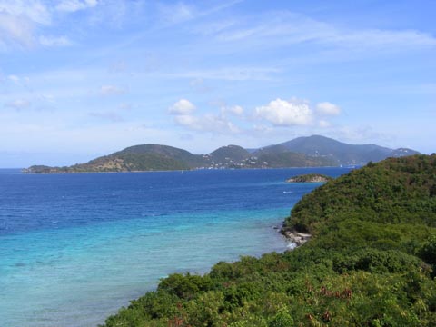 The green tree-covered shore
       runs diaagonally on the right side of the photo. The blue color of the
       bay water deeps as you look away from the shore. Waterlemon
       Cay is a small green spot sticking out from the shore. Little
       Thatch Island rises from the water near the horizon. Tortola is
       partially behind Little Thatch Island, but buildings are visible
       on its hillsides.