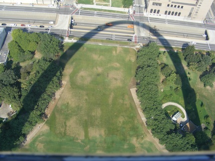 The shadow of the Arch curves           across the park at its base and onto the Interstate highway           below