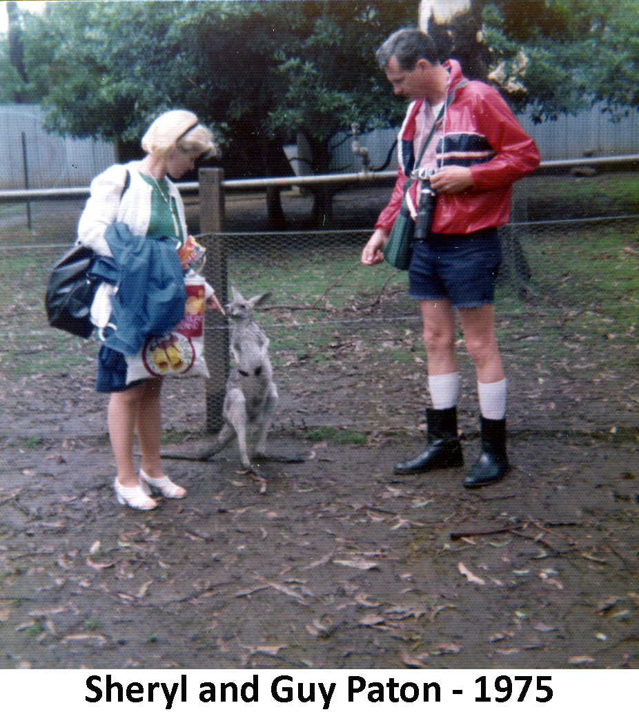 Sheryl and Guy Paton feeding treats to a wallaby, that stands      about thigh-high between them. Theres a fence and a tree behind them.