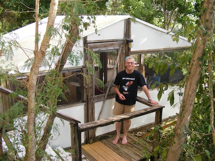 Al, wearing a Kepler
            T-shirt and shorts, stands in front of the door to the
            canvas and screen cabin. Trees surround the scene.