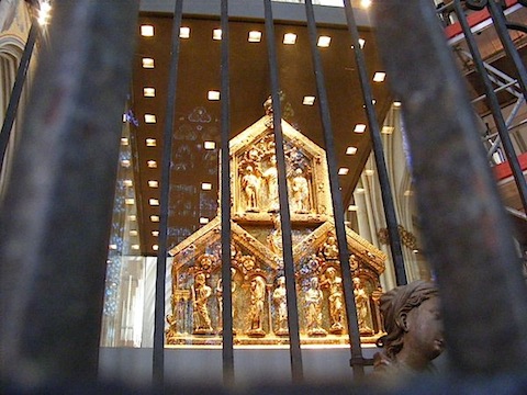 Seen through bars and glass (in which the stained glass windows              behind the camera are reflected) is a pyramid formed by three              gold pentagons, each featuring a Biblical scene.