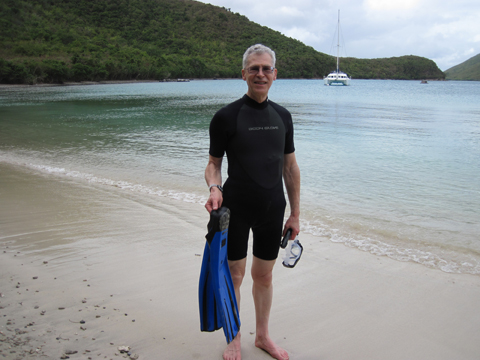 Al is standing on the shore
          at Waterlemon Bay with the water and a catamaran in the
          background. He is wearing a black, short wet suit and
          carrying his blue swim fins and his snorkel and mask.
          The sky is mostly cloudy.