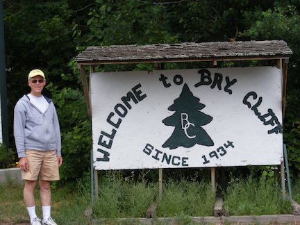 Al stands alongside the sign that
               says we welcome you to Bay Cliff, established 1934