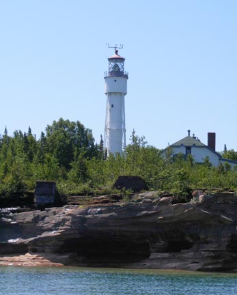 The photo was taken from a boat on Lake
                  Superior. The lighthouse is a simple, white
                  cylinder above a cliff.