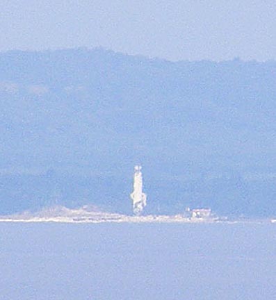 The white tower is visible in the middle of the
               photo. Haze makes the island look blue.