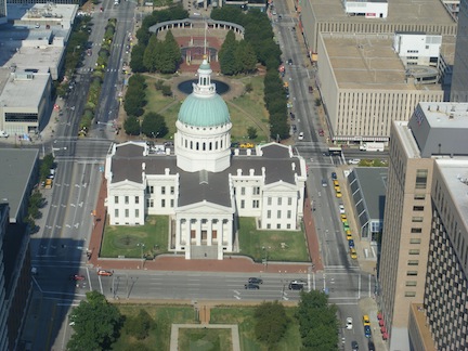 The white courthouse      has four wings and a green dome. It sits in parkland amidst office     buildings