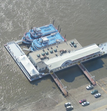 Two riverboats are          docked at the riverboat cruise wharf. Their upper decks are         blue. The water is muddy.