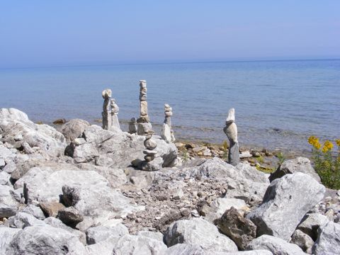 Six or Seven piles of rocks on the rocky shore
               of Lake Huron. The blue water and blue sky.